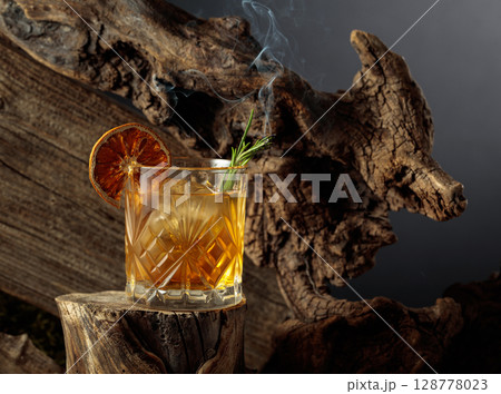 An old-fashioned cocktail over ice on an old wooden stump. 128778023
