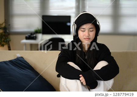 Sad teenage girl at home, listening to music with a serious expression. Mental health concept Sad teenage girl at home, listening to music with a serious expression. Mental health concept 128779419