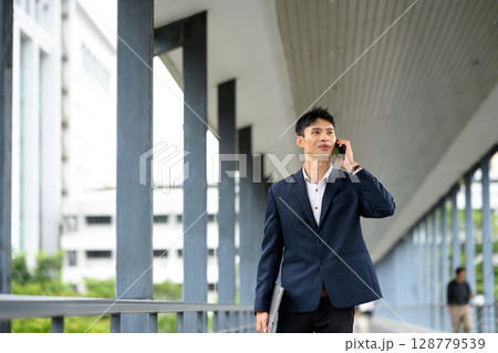 Confident businessman talking on the phone while walking in the city Confident businessman talking on the phone while walking in the city 128779539