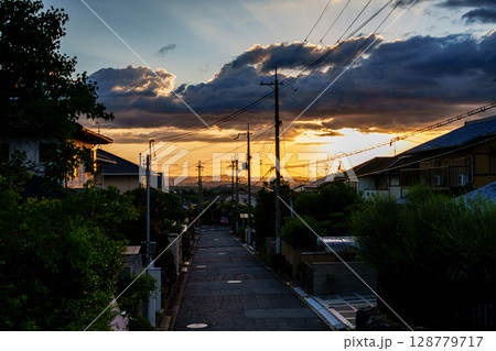 山際の空を黄金色に染めながら奈良市街地に沈んで行く夕日　電柱が立ち並ぶ市道と夕焼け空② 128779717