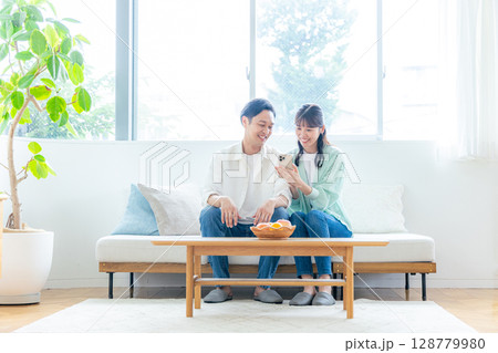 リビングでスマホを見る若い夫婦 128779980