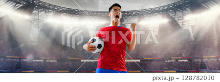 Football player in red shirt celebrating with ball in crowded 3D stadium 128782010