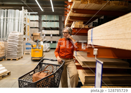Woman shopping for home improvement supplies in a large hardware store with various departments 128785729
