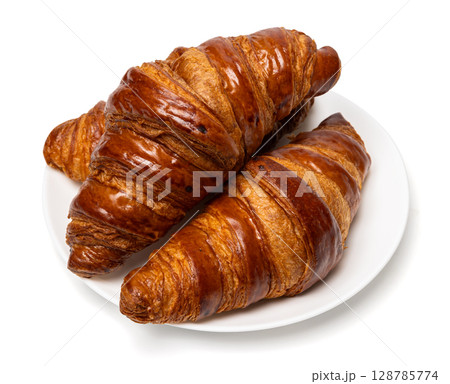 Three freshly baked classic delicious fresh organic croissants on white ceramic plate isolated on white background Three freshly baked classic delicious fresh organic croissants on white ceramic plate isolated on white background 128785774