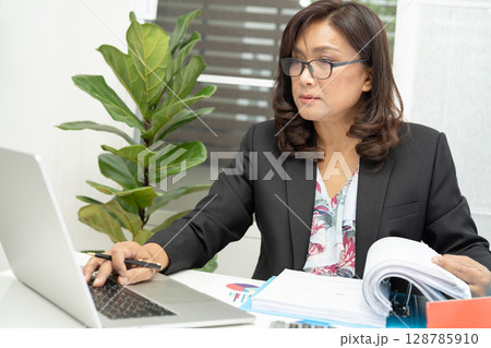 Asian accountant working and analyzing financial reports project accounting with chart graph and calculator in modern office, finance and business concept. Asian accountant working and analyzing financial reports project accounting with chart graph and calculator in modern office, finance and business concept. 128785910