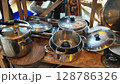Collection of assorted metallic cooking pots and pans displayed on a rustic wooden shelf at a flea market in a lively urban setting 128786326