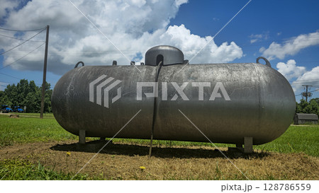 Large industrial propane tank installed outdoors on grass, designed for fuel storage and efficiency. The tank showcases durability and purpose for various industries and homes Large industrial propane tank installed outdoors on grass, designed for fuel storage and efficiency. The tank showcases durability and purpose for various industries and homes 128786559