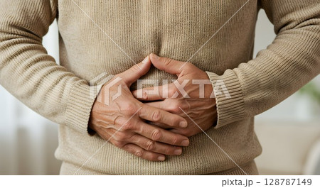 Man clutching stomach in pain. Abdominal discomfort and digestive health issue. Healthcare and medical concept for wellness. Man clutching stomach in pain. Abdominal discomfort and digestive health issue. Healthcare and medical concept for wellness. 128787149