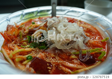 Spicy Korean seafood cold noodle soup (Mulhoe) with fresh squid sashimi in large bowl 128787519