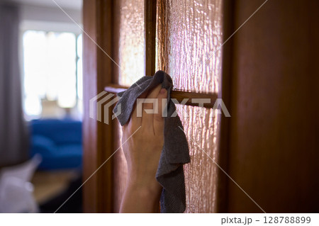 Carefully Hand Cleaning a Sparkling Glass Door with a Soft Sponge in the Kitchen Area 128788899