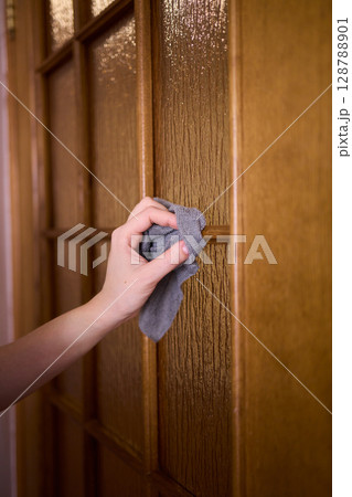 Carefully Hand Cleaning a Sparkling Glass Door with a Soft Sponge in the Kitchen Area 128788901