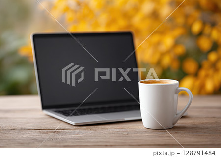 Laptop and coffee cup on wooden table with blurred yellow background create cozy autumn atmosphere Laptop and coffee cup on wooden table with blurred yellow background create cozy autumn atmosphere 128791484