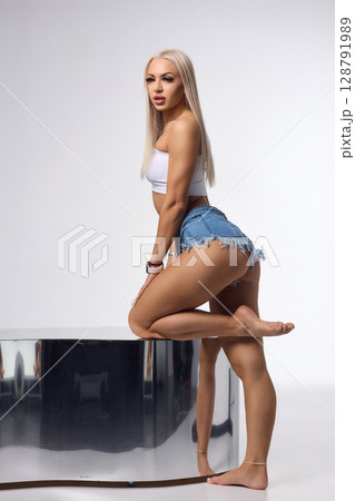 A Stylish and Fashionable Model Posing Confidently in Denim Shorts with Long, Flowing Blonde Hair 128791989