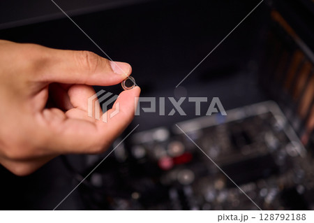 A Hand Holding a Small Electronic Component Close to a Computer Motherboard for Setup A Hand Holding a Small Electronic Component Close to a Computer Motherboard for Setup 128792188