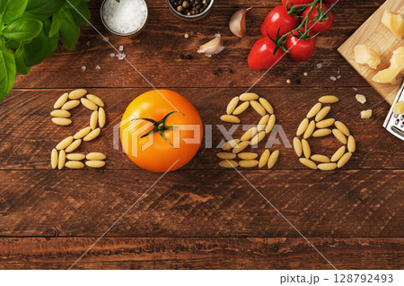 Date 2026 made of pasta with yellow tomatoes on a rustic wooden background, with garlic, cheese, herbs, and tomatoes. 128792493