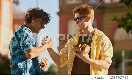 Two male friends shaking hands while holding sandwiches outdoors in summer Two male friends shaking hands while holding sandwiches outdoors in summer 128792751