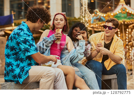 Young people eating wraps and chatting near amusement ride Young people eating wraps and chatting near amusement ride 128792775
