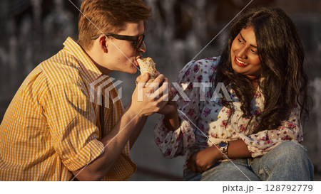 Two friends relishing takeout meal outside during sunset Two friends relishing takeout meal outside during sunset 128792779