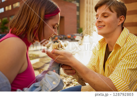Young couple enjoying street food near city fountain on a sunny day 128792803