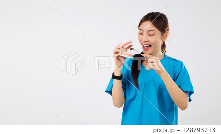 Asian woman smiling, dental model holding mirror, showing teeth in clinic, medical nurse displays oral tool, this dental demonstration ensures healthy gums and teeth, isolated studio white background 128793213
