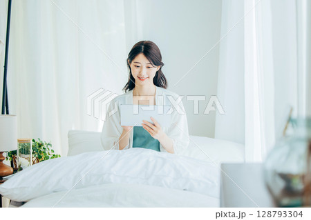 ベッドでタブレットを操作するミドルの女性 ベッドでタブレットを操作するミドルの女性 128793304