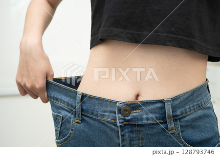 Young Asian woman losing weight wearing loose pants in oversize jeans. 128793746