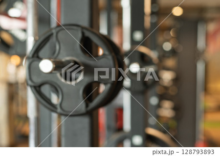Abstract blurred gym background with sports fitness equipment barbell and weight plates in defocus. Sport background with space for design. 128793893