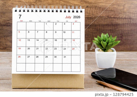 July 2026 desk calendar on wooden table with black smartphone. July 2026 desk calendar on wooden table with black smartphone. 128794425