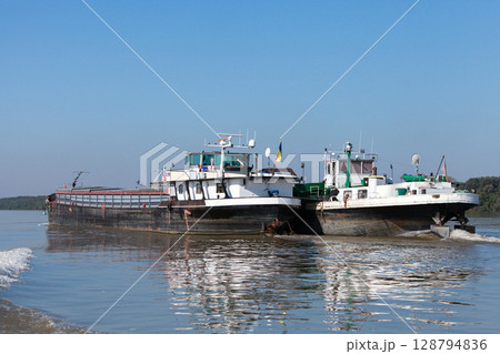 Cargo Ships Cruising Downriver Under a Clear Blue Sky 128794836