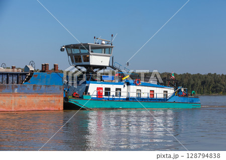 A blue and white tugboat moves a barge on Danube river, 128794838