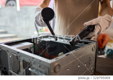 A man cleans a computer case with a vacuum in a bright room, stressing workspace tidiness 128795009