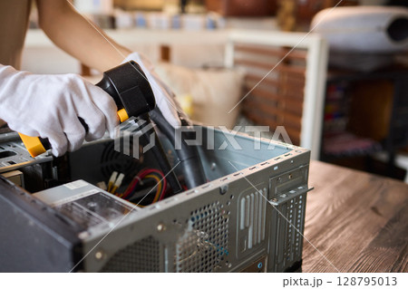 A man cleans a computer case with a vacuum in a bright room, stressing workspace tidiness 128795013