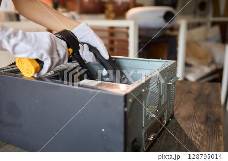 A man cleans a computer case with a vacuum in a bright room, stressing workspace tidiness A man cleans a computer case with a vacuum in a bright room, stressing workspace tidiness 128795014
