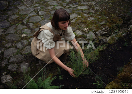 A woman with gray hair sits peacefully while reading a book in a humid subtropical environment. The tall grass sways gently around her, creating a serene atmosphere 128795043