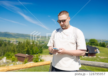 Man Using Smartphone Outdoors with Scenic Mountain View Man Using Smartphone Outdoors with Scenic Mountain View 128795957