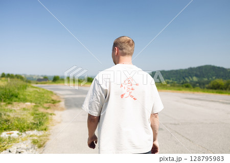 Man Walking Along Road in Countryside on Sunny Day 128795983