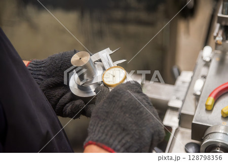 Close up scene the machine operator measuring dimension of metal shaft parts by dial Vernier caliper. 128798356