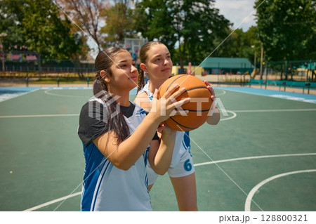 Female athletes training on an outdoor basketball court beneath a sunny sky 128800321