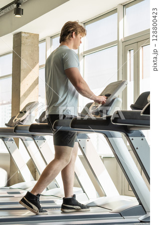 Young caucasian man running track, warming up on treadmill at fitness center. Cardio workout. Close up. 128800423