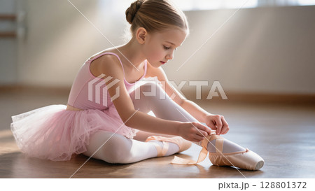 Little ballerina in pink tutu ties her pointe shoes while preparing for ballet class in a sunlit dance studio. Graceful childhood moment. Little ballerina in pink tutu ties her pointe shoes while preparing for ballet class in a sunlit dance studio. Graceful childhood moment. 128801372