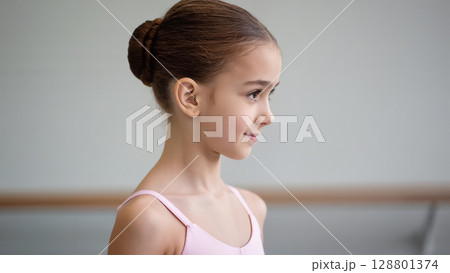 Portrait of a young ballerina in a pink leotard with a neat bun, standing in a dance studio. Graceful and focused expression. Portrait of a young ballerina in a pink leotard with a neat bun, standing in a dance studio. Graceful and focused expression. 128801374