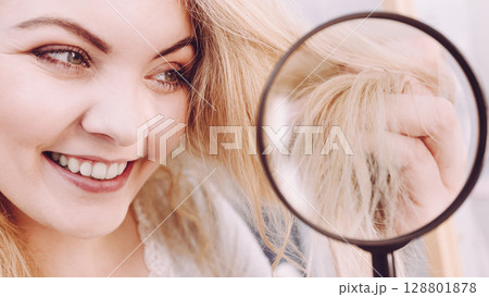 Woman looking at hair ends through magnifying glass 128801878
