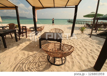 Seating area under a canopy on a sunny beach with a person enjoying the ocean view in the popular summer travel destination in Koh Rong Sanloem, Sihanoukville, Cambodia 128801959