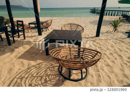 Wicker chairs and a table on sandy beach facing the turquoise ocean in Koh Rong Sanloem, Sihanoukville, Cambodia 128801960