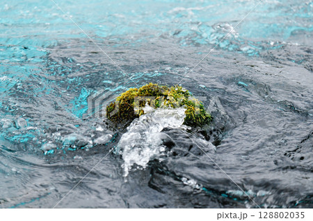 Moss-covered rock in pure Icelandic stream with swirling water. Concept of sustainability, minimalism, environmental balance, clean energy and fragile natural beauty. Moss-covered rock in pure Icelandic stream with swirling water. Concept of sustainability, minimalism, environmental balance, clean energy and fragile natural beauty. 128802035