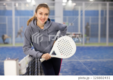Portrait of a young woman tennis player standing with a padel racket Portrait of a young woman tennis player standing with a padel racket 128802431