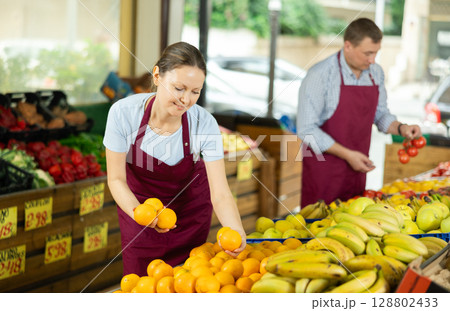 Positive saleswoman in apron offering oranges on supermarket 128802433