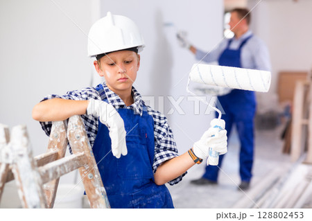 Portrait of boy with paint roller who helps his father to renovate room Portrait of boy with paint roller who helps his father to renovate room 128802453