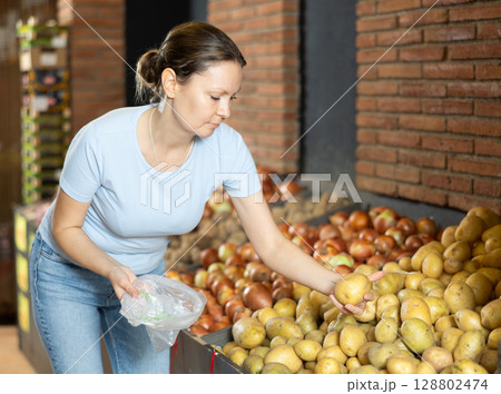 Woman purchaser choosing potatoes at counter in large grocery store 128802474