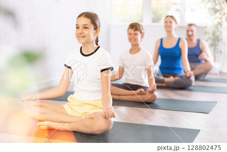 Pleasant preteen girl practicing lotus pose of yoga with her family 128802475